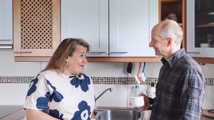 Mies ja nainen keskustelevat iloisesti keittiössä kahvikupit kädessään.